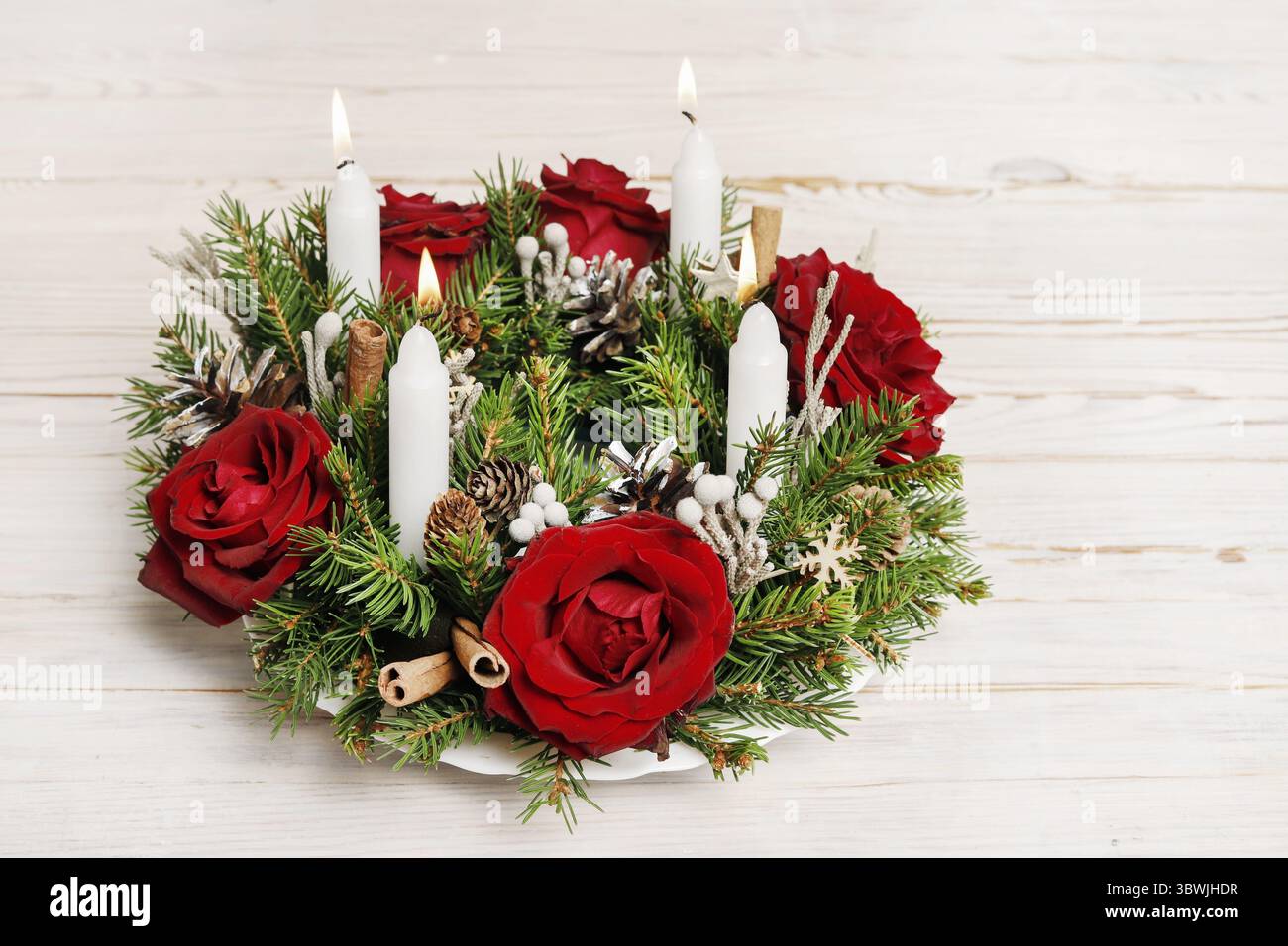 Florist bei der Arbeit: Wie man einen traditionellen Adventskranz für den Tisch aus Rosenblüten, Tannenzweigen und zusätzlichen Elementen bastelt. Stockfoto