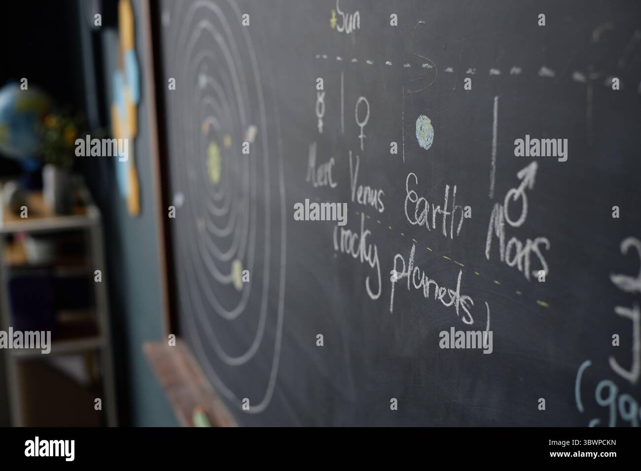 Tafel mit handgezeichnetem Sonnensystem-Diagramm mit beschrifteten Planeten und Umlaufbahnen, im Hintergrund sichtbarer Unterrichtsraum, pädagogisches Konzept für astronomisches Lernen Stockfoto