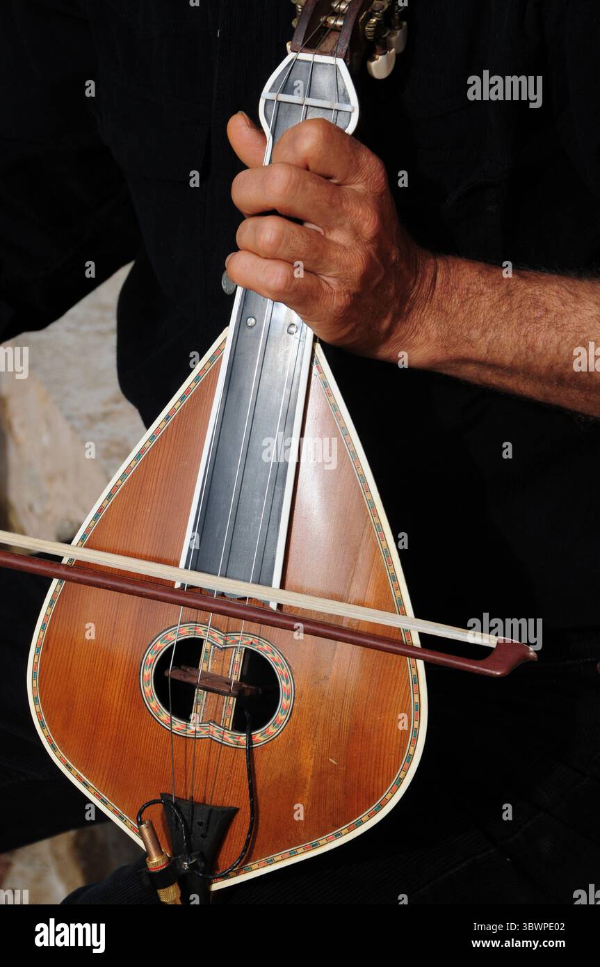 Eine Person spielt geschickt ein traditionelles Streichinstrument, kretische Lyra, wobei eine Hand den Hals hält und die andere einen Bogen über die Saiten zieht. Stockfoto Eine Person spielt geschickt ein traditionelles Streichinstrument, kretische Lyra, wobei eine Hand den Hals hält und die andere einen Bogen über die Saiten zieht. Stockfoto