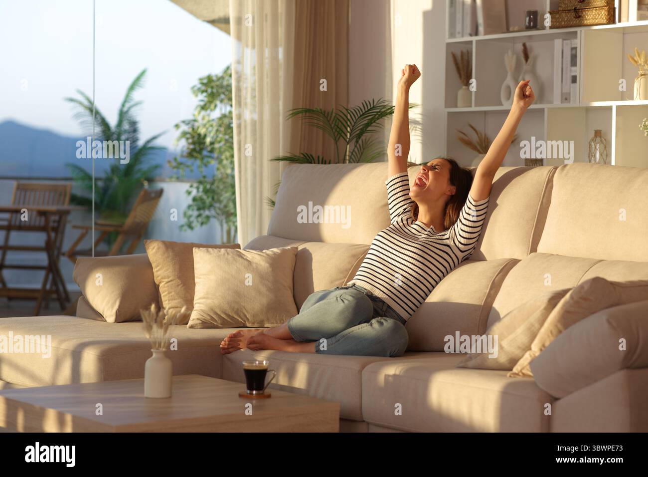 Aufgeregte Frau, die zu Hause auf einer Couch sitzt Stockfoto