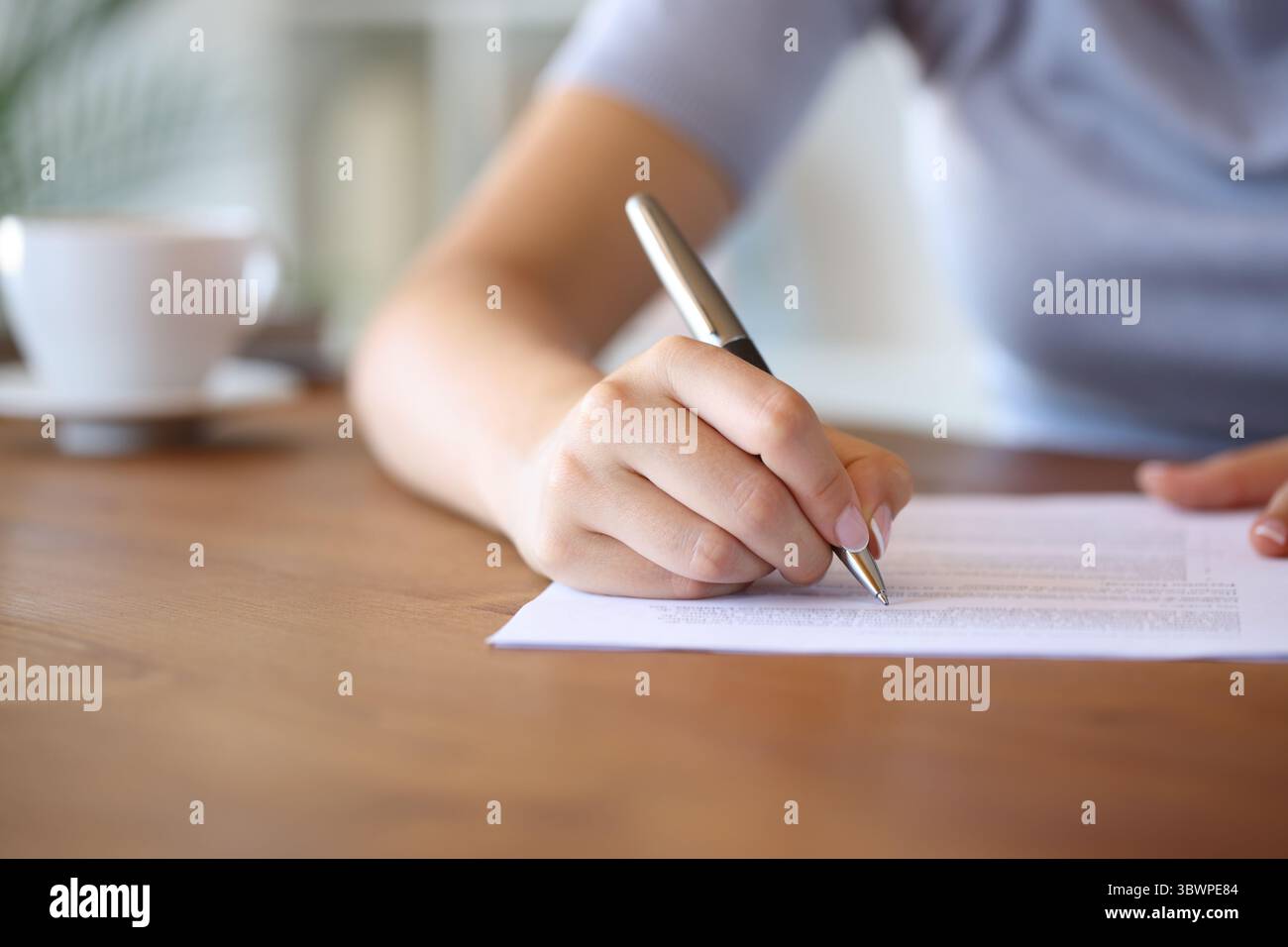 Nahaufnahme einer Frau, die zu Hause auf einem Holztisch auf Papier schreibt Stockfoto
