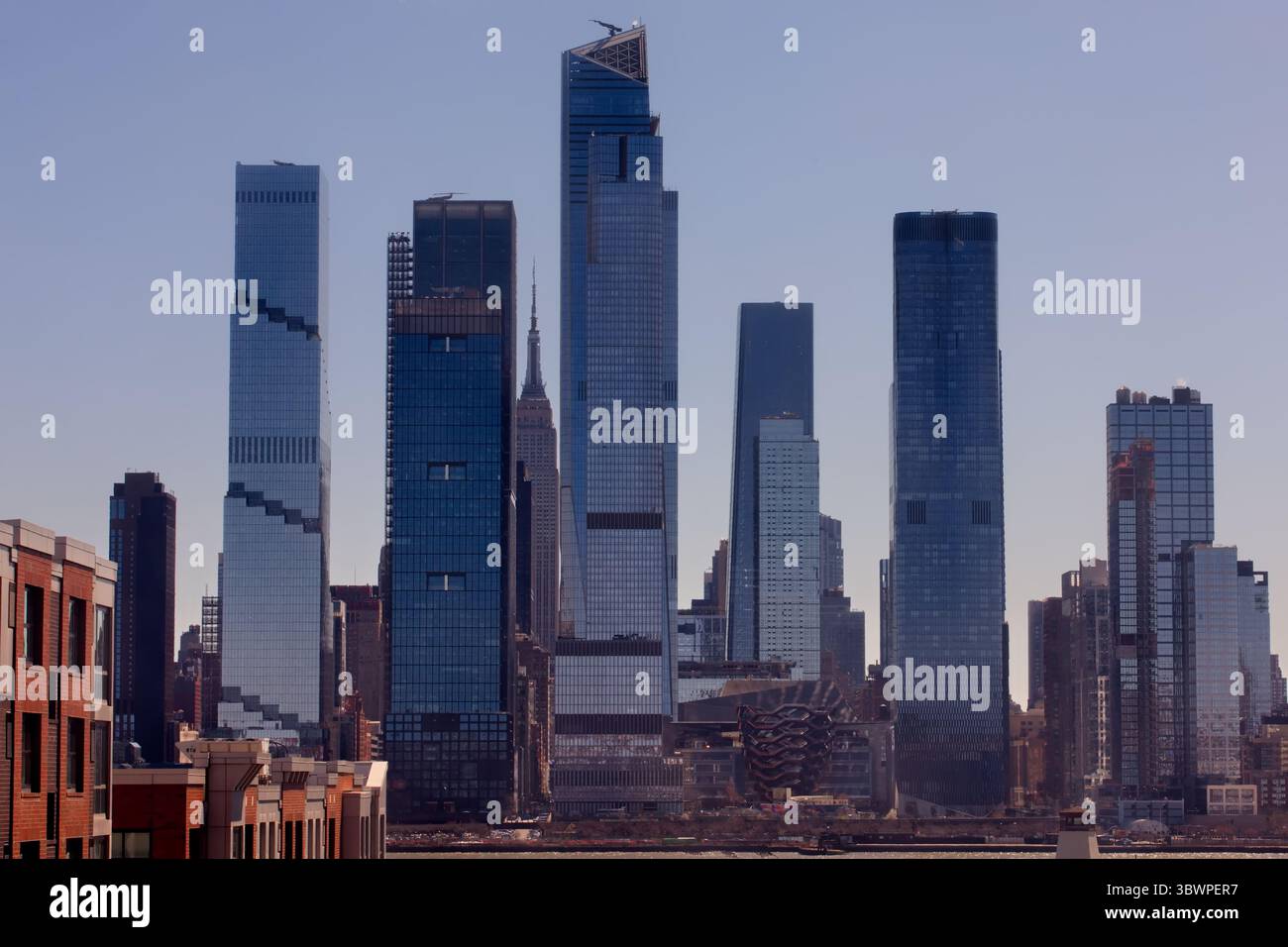 Die sonnendurchfluteten Wolkenkratzer von Midtown Manhattan funkeln über dem Hudson River, während Jersey City die legendäre Skyline von New York heute in einem pulsierenden Stadtpanorama umrahmt. Stockfoto