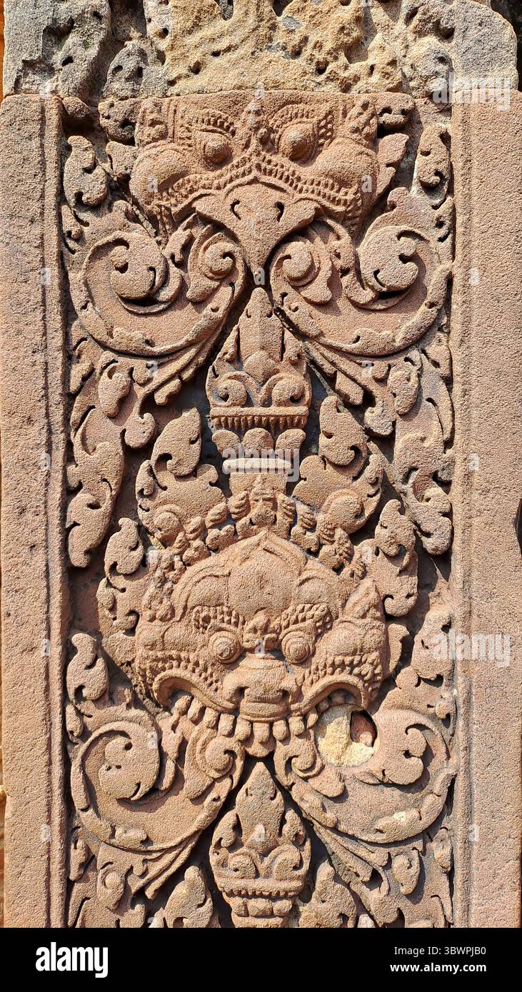 Nahaufnahme der Sandsteinschnitzerei im Banteay Srei Tempel in Siem Reap, Kambodscha, mit mythologischem Schutzgesicht und Blumenschmuck in klassischen Khmer s Stockfoto