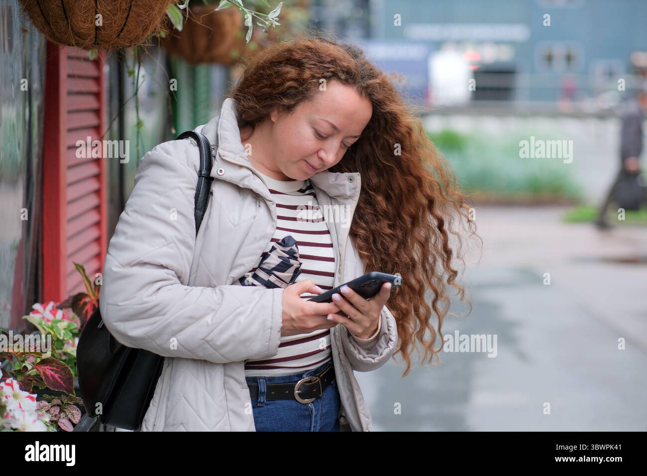 Die junge Frau genießt einen Moment der Verbindung auf einem regnerischen Bürgersteig. Stockfoto