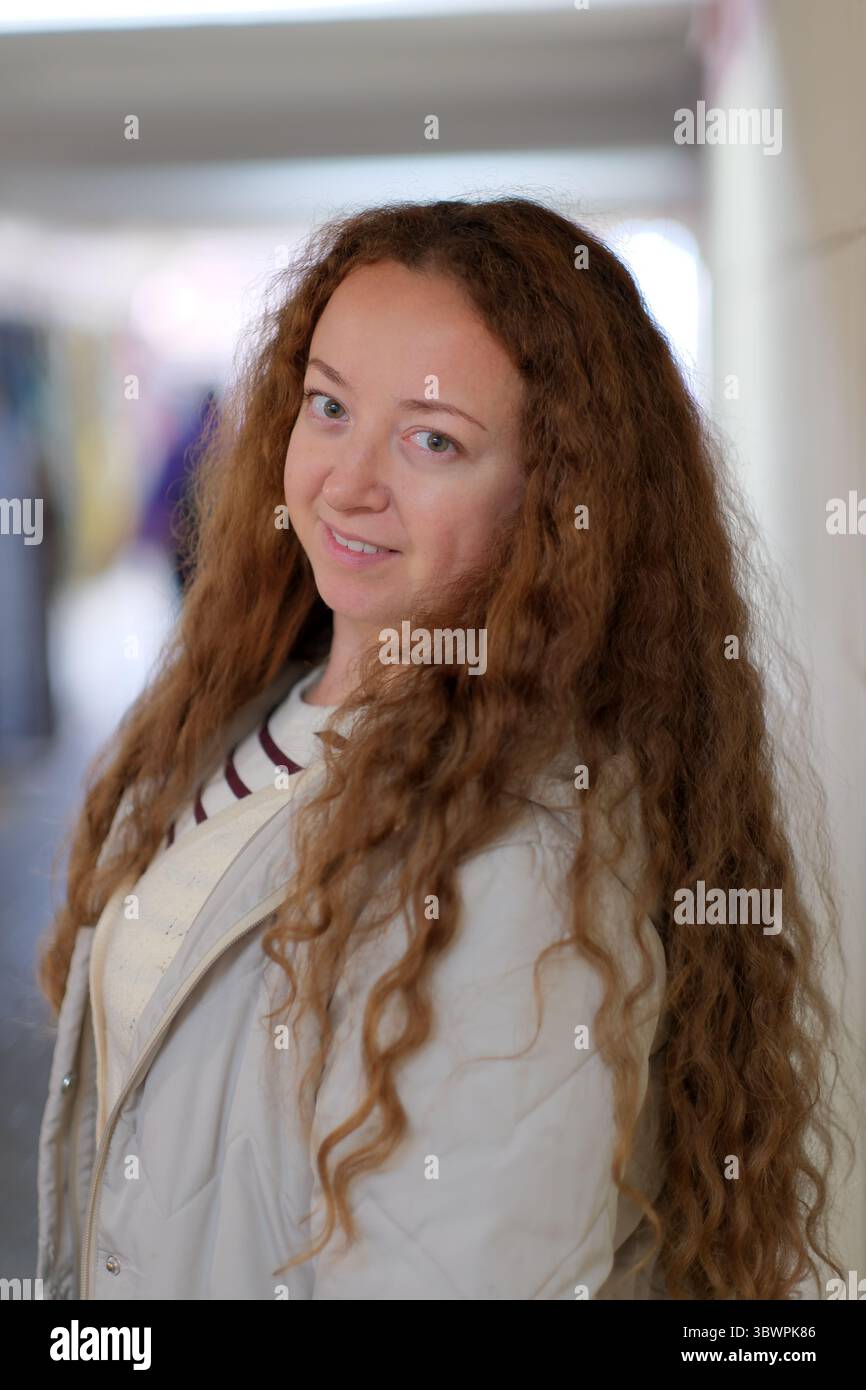 Eine Frau mit leuchtenden lockigen Haaren steht lächelnd in einem sanft beleuchteten Flur und strahlt Wärme aus. Stockfoto