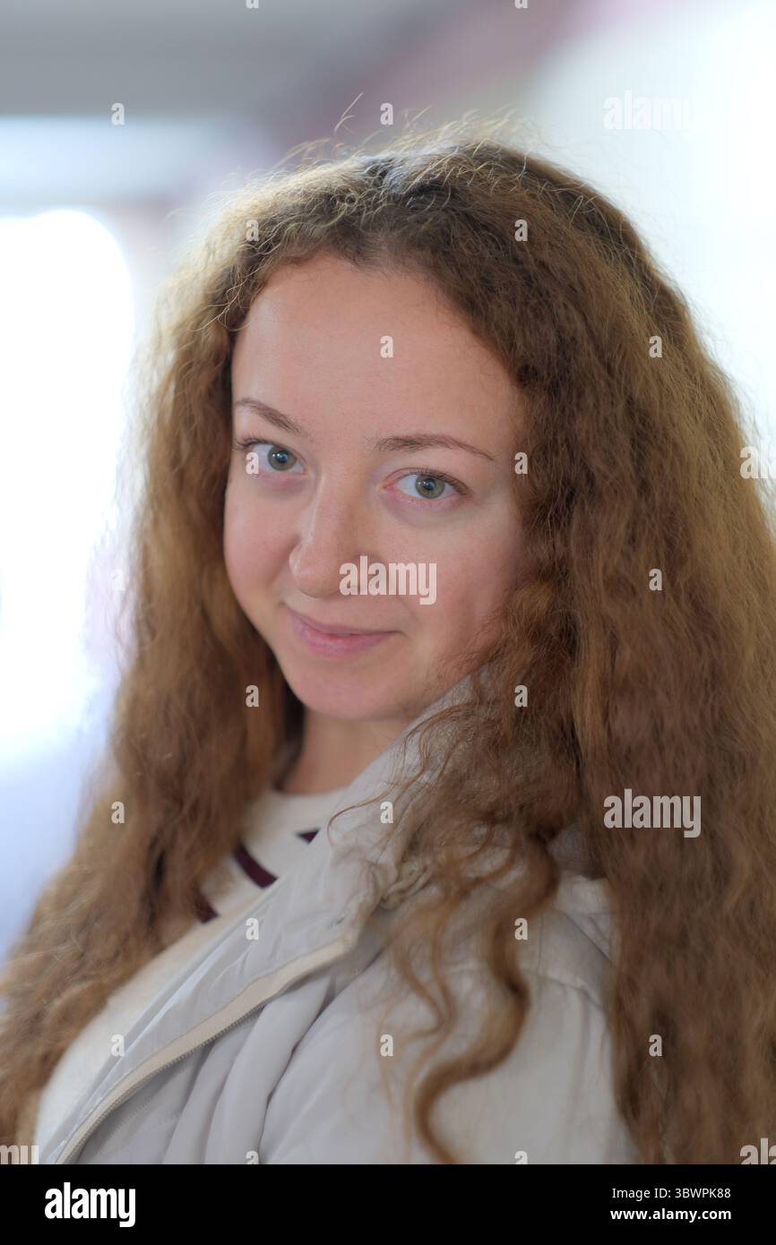 Eine junge Frau mit lockigen Haaren steht in einem Flur und strahlt Ruhe und Gelassenheit aus. Stockfoto