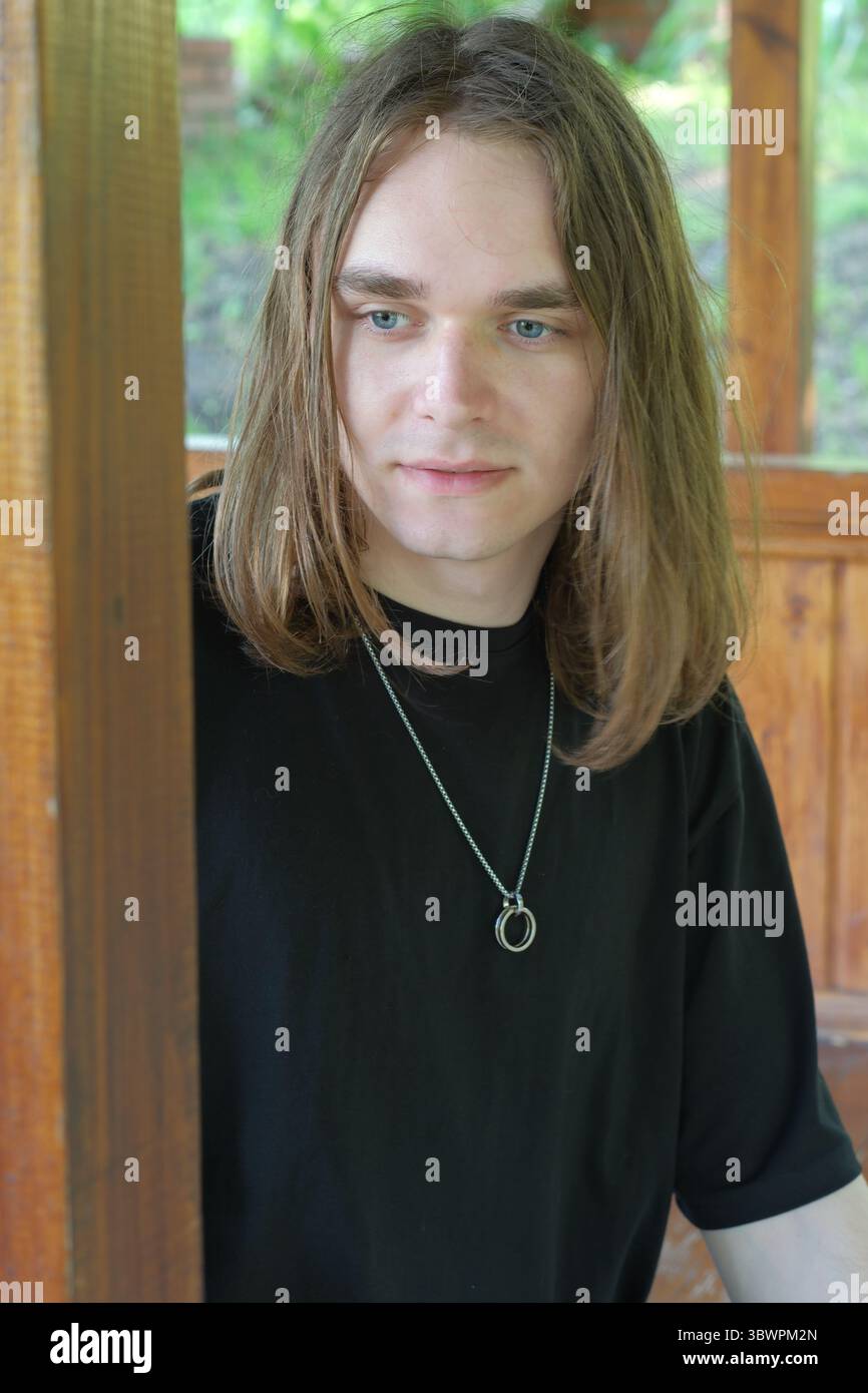 Ein junger Mann mit langen Haaren steht still in einer Kabine, verloren in Reflexion. Stockfoto