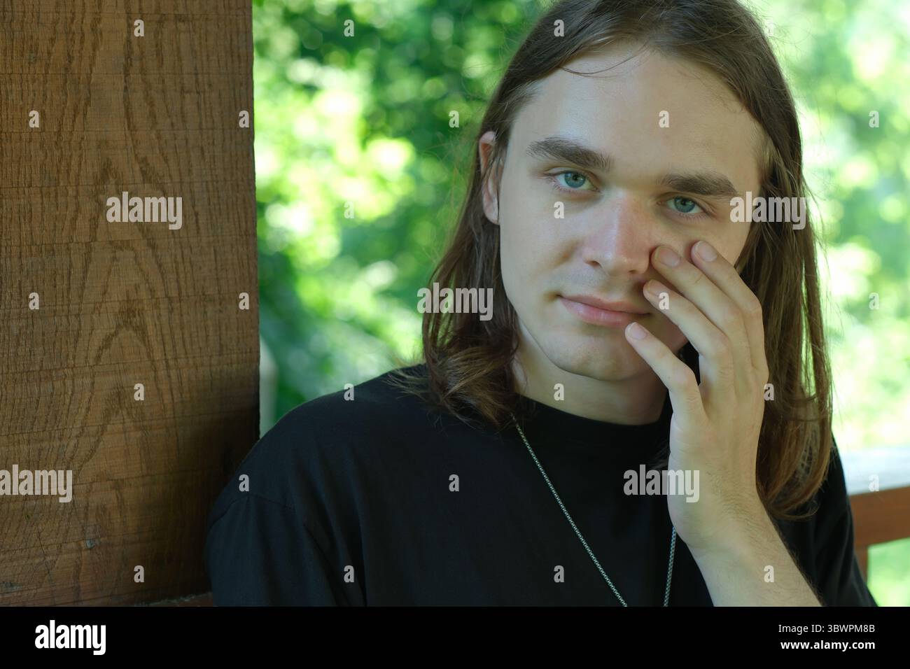 Ein junger Mann berührt sanft sein Gesicht, während er sich draußen in Gedanken verirrt. Stockfoto