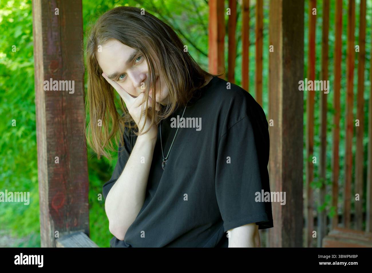 Eine Person mit langen Haaren steht nachdenklich in einer lebhaften grünen Umgebung. Stockfoto