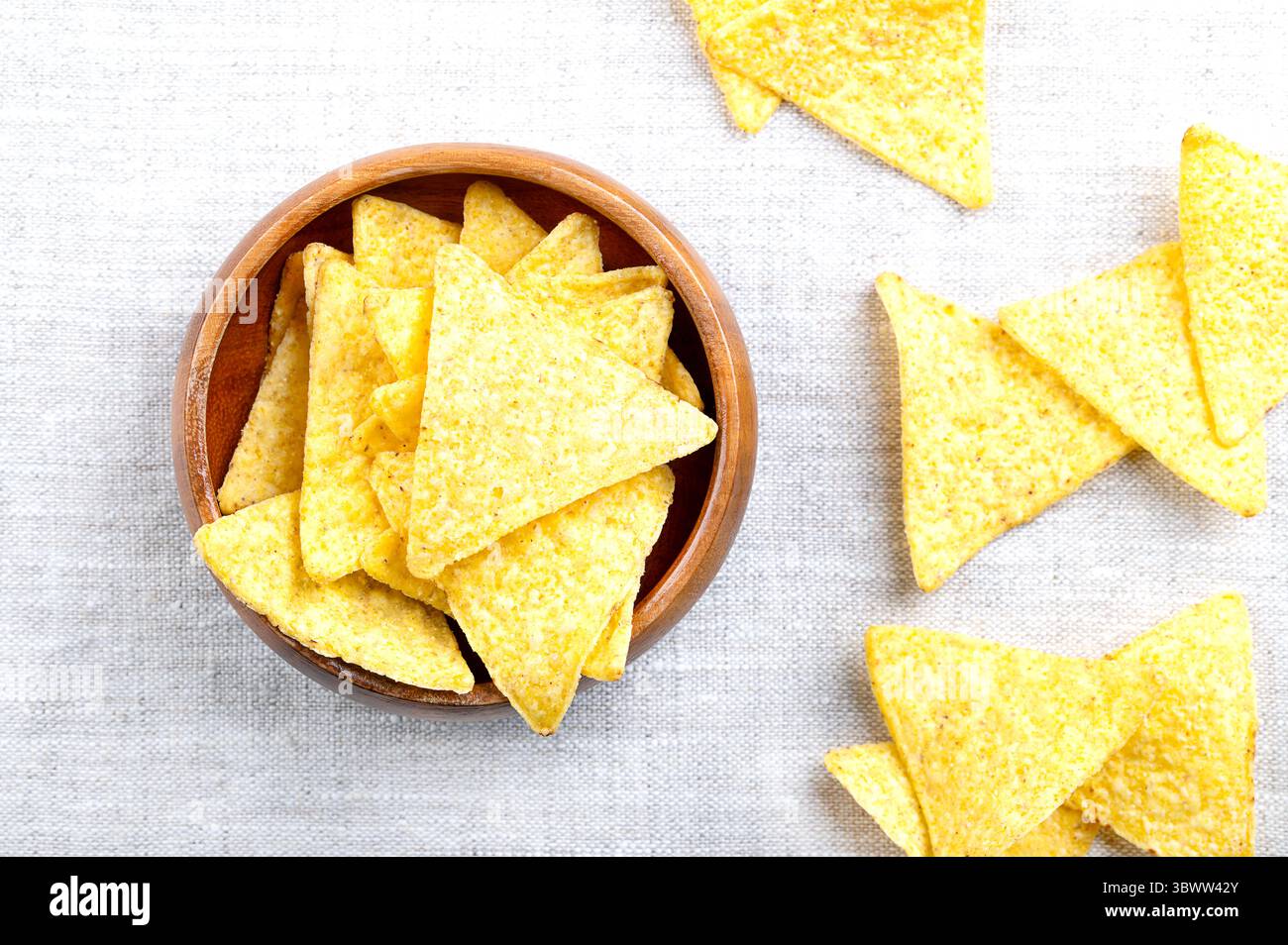 Tortillachips in einer Holzschale auf Leinen. Klassische, knusprige Snacks aus Maistortillas, in dreieckige Keile geschnitten, in Öl frittiert. Stockfoto