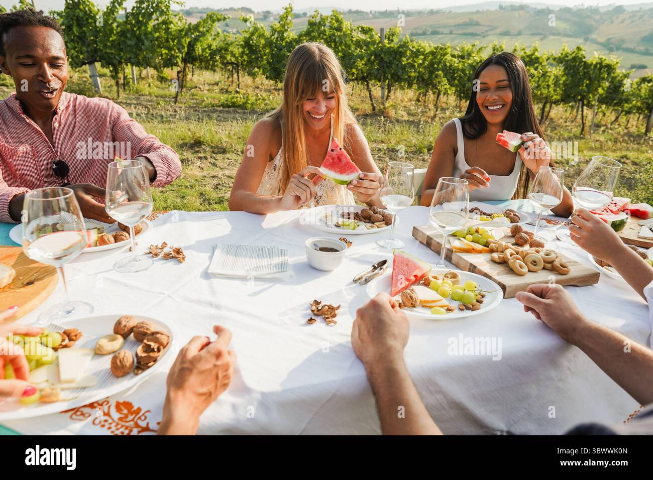 Glückliche multirassische Freunde essen Wassermelone im Freien, während sie weißes Weinen im ländlichen Resort trinken - Sommer Lifestyle und Urlaubskonzept - Main Fo Stockfoto