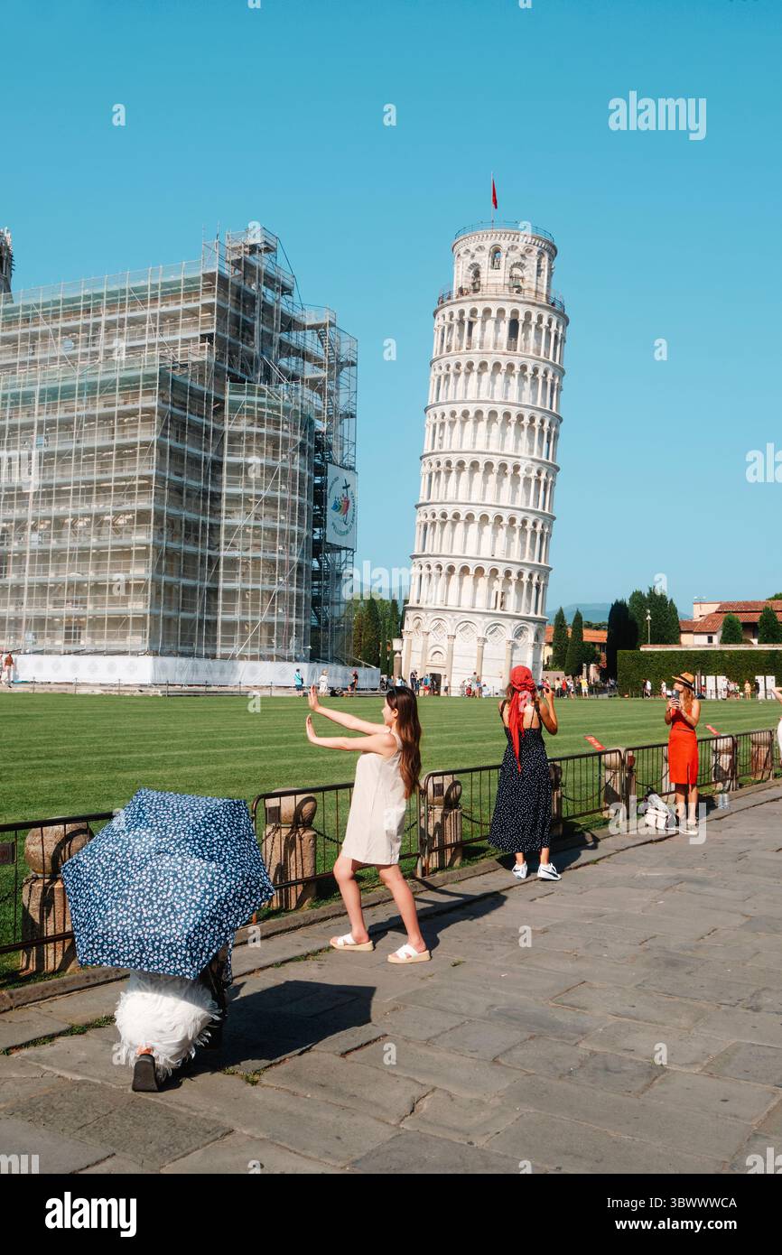 Pisa, Italien - 26. Juni 2025: Eine junge Frau in einem weißen Kleid posiert, als würde sie den Schiefen Turm von Pisa aufrichten, während andere um sie herum streiken Stockfoto