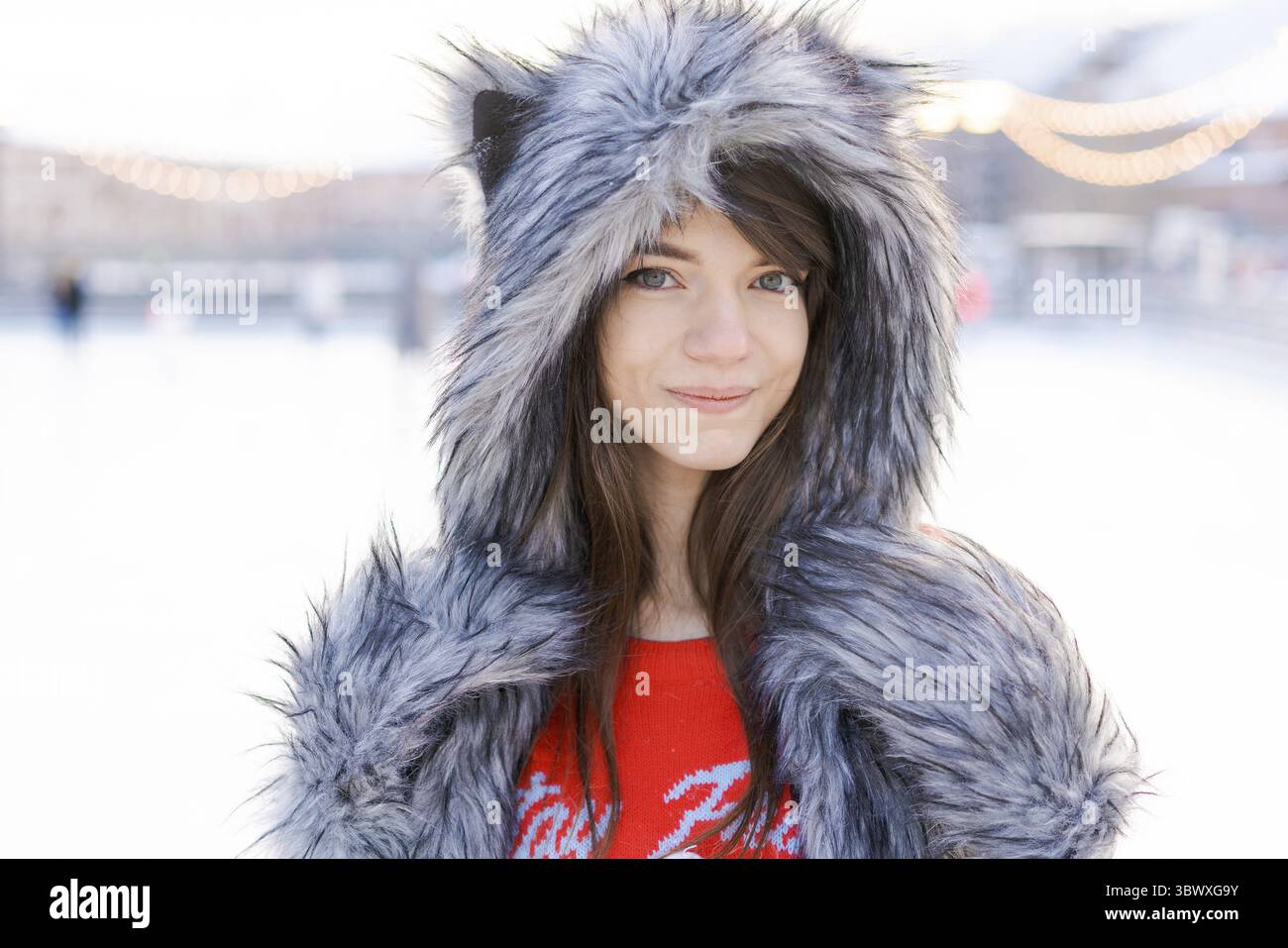 Portrait niedliche junge Frau im zotteligen Hut mit Ohren blickt auf die Kamera und lächelt an einem sonnigen frostigen Tag vor dem Hintergrund einer Eiskatze im Winter Stockfoto