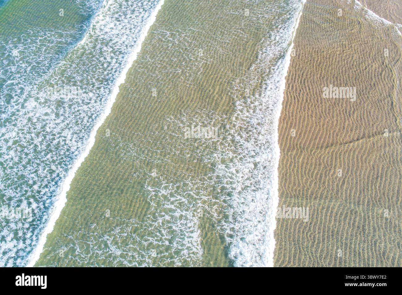 Luftaufnahme der Ozeanwellen, die über einem gewellten Sand Beach von oben nach unten über die Drohne springen Stockfoto