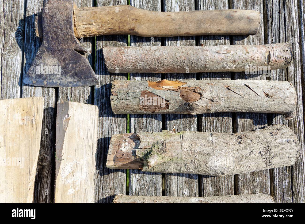 Ein Bild von einer alten Axt und mehreren Baumstämmen, die auf verwitterten Holzdielen angeordnet sind, heben Texturen und ein rustikales Thema hervor. Stockfoto