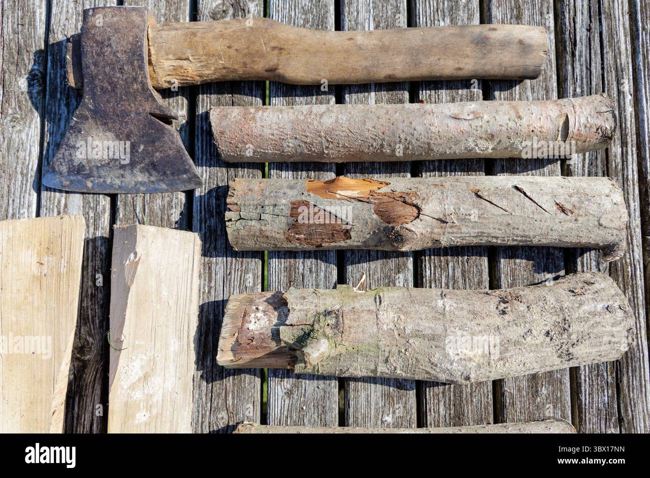 Ein Bild von einer alten Axt und mehreren Baumstämmen, die auf verwitterten Holzdielen angeordnet sind, heben Texturen und ein rustikales Thema hervor. Stockfoto