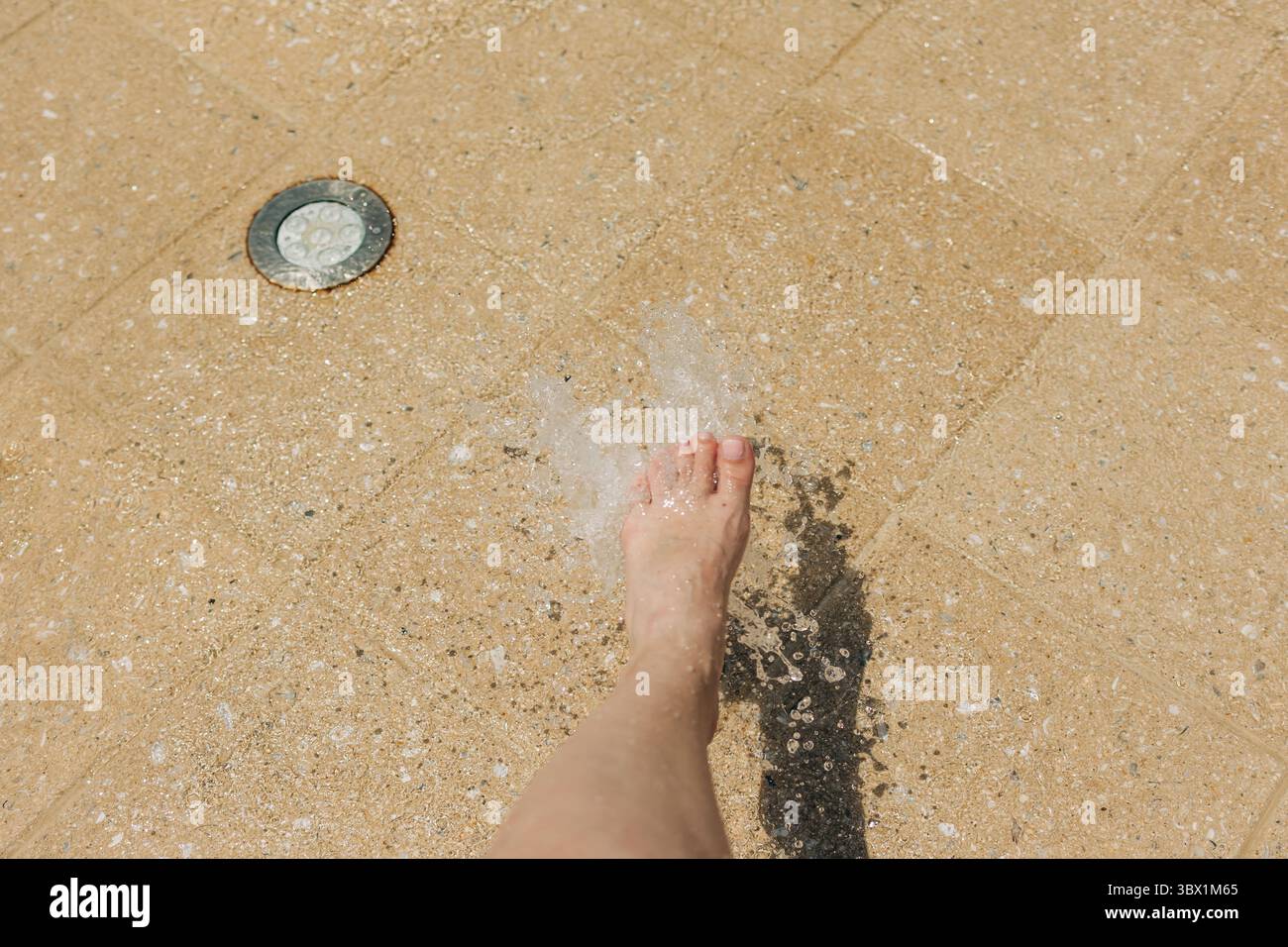Ein Fuß tritt ins spritzende Wasser und genießt die Kühle an einem hellen Tag in einem Wasserspielplatz. Stockfoto