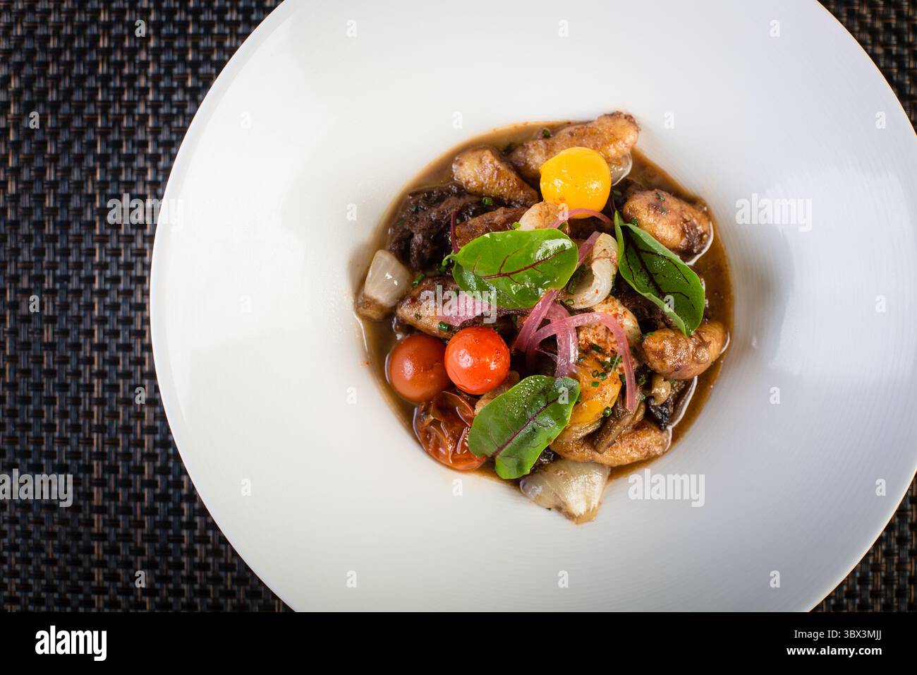 Elegante Gnocchi mit gemischtem Gemüse und Kirschtomaten auf einem achteckigen weißen Teller. Feine italienische Kartoffelknödel mit frischen Kräutern. Stockfoto