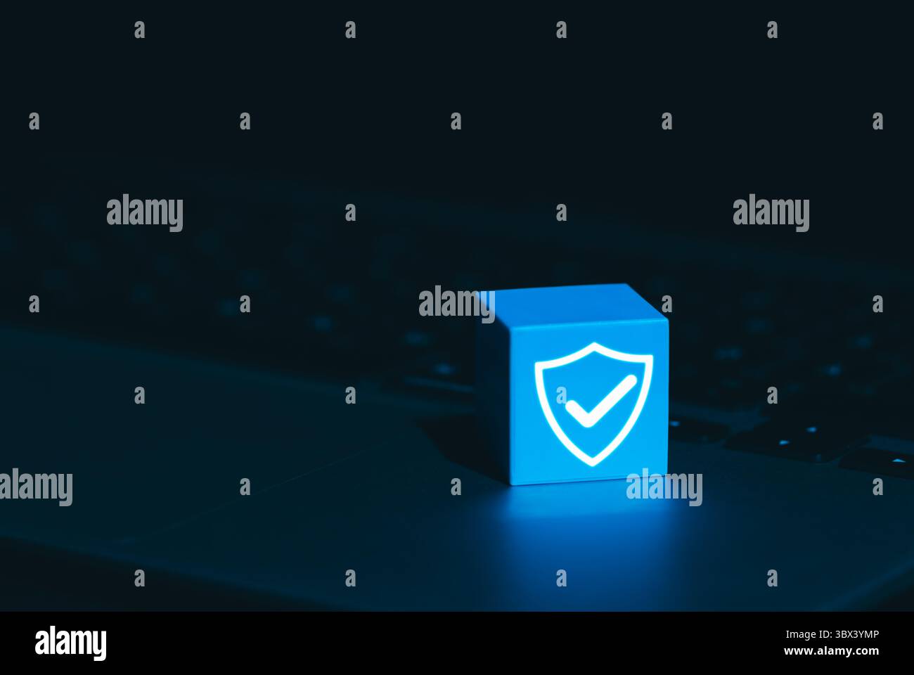 Symbol für Cybersicherheit und Datenschutz. Ein leuchtend blauer Würfel mit Schild und Häkchen auf der Laptop-Tastatur, der Cyber-Sicherheit symbolisiert, Stockfoto