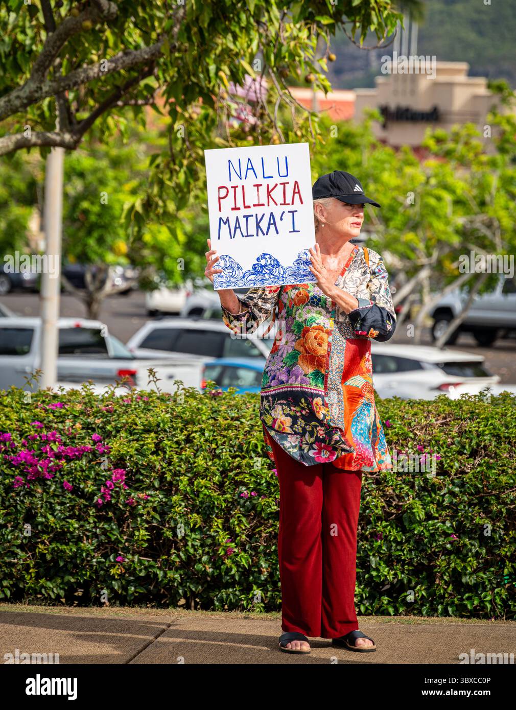 Ein Demonstrant mit einem Schild, das „gute Wellen angesichts der Schwierigkeit“ bedeutet (ungefähr „macht gute Ärger“), auf dem Bürgersteig bei einer Kundgebung im Kukui Grove. Stockfoto