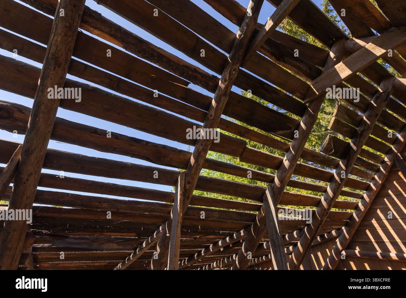 Aus nächster Nähe ein rustikales Holzgebäude mit freiliegenden Balken und offenem Dach. Sonnenlicht filtert durch die Lücken und erzeugt ein helles und natürliches Licht Stockfoto