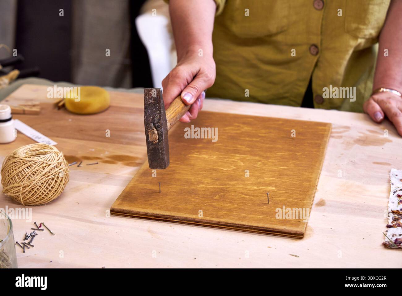 Nahaufnahme einer Frau, die Nägel in ein gebeiztes Holzbrett hämmert, für handgefertigte Dekorationen. Teil eines umweltfreundlichen DIY-Wandpaneelprojekts mit Naturpapier und Ma Stockfoto