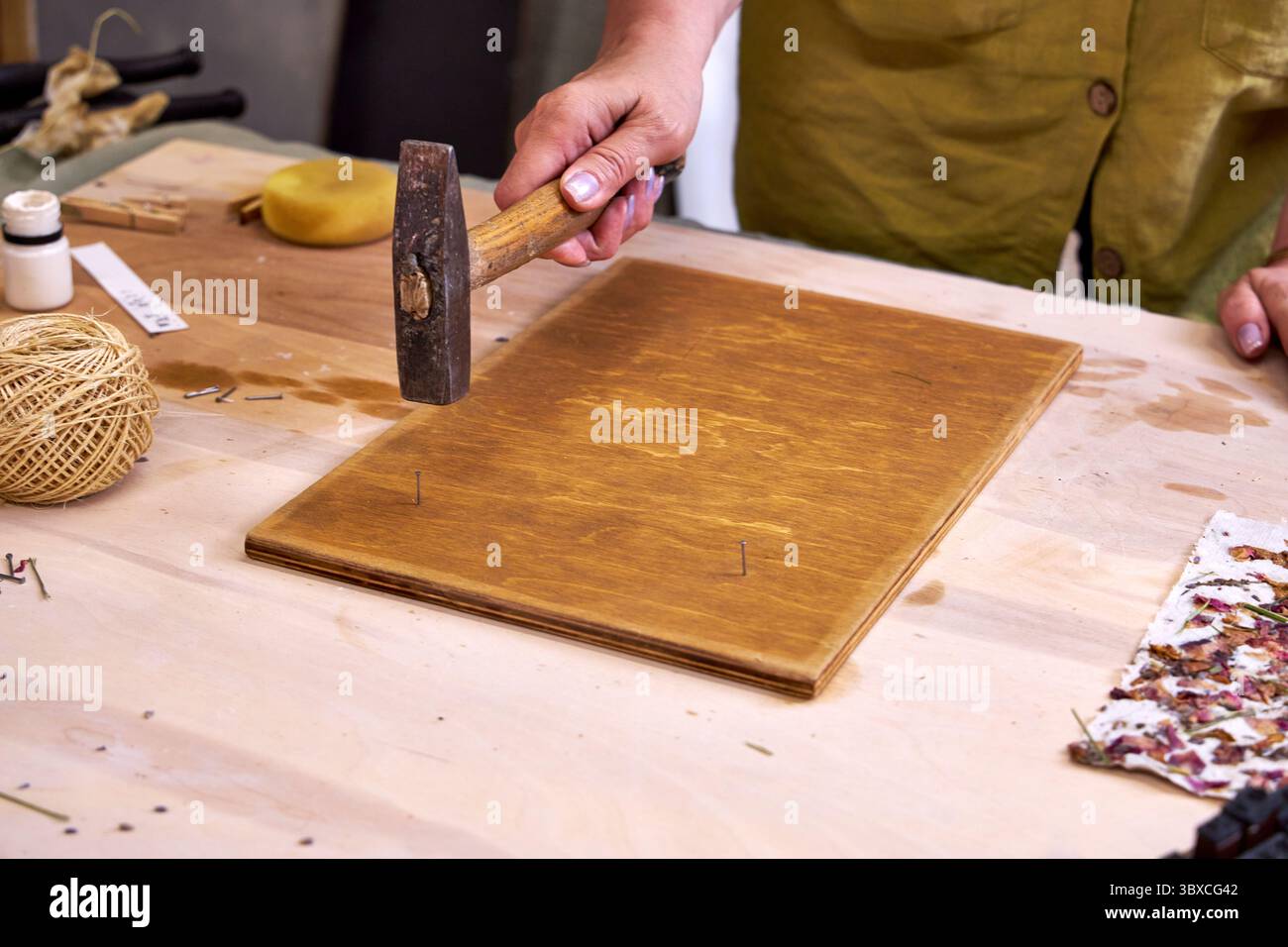 Nahaufnahme einer Frau, die Nägel in ein gebeiztes Holzbrett hämmert, für handgefertigte Dekorationen. Teil eines umweltfreundlichen DIY-Wandpaneelprojekts mit Naturpapier und Ma Stockfoto