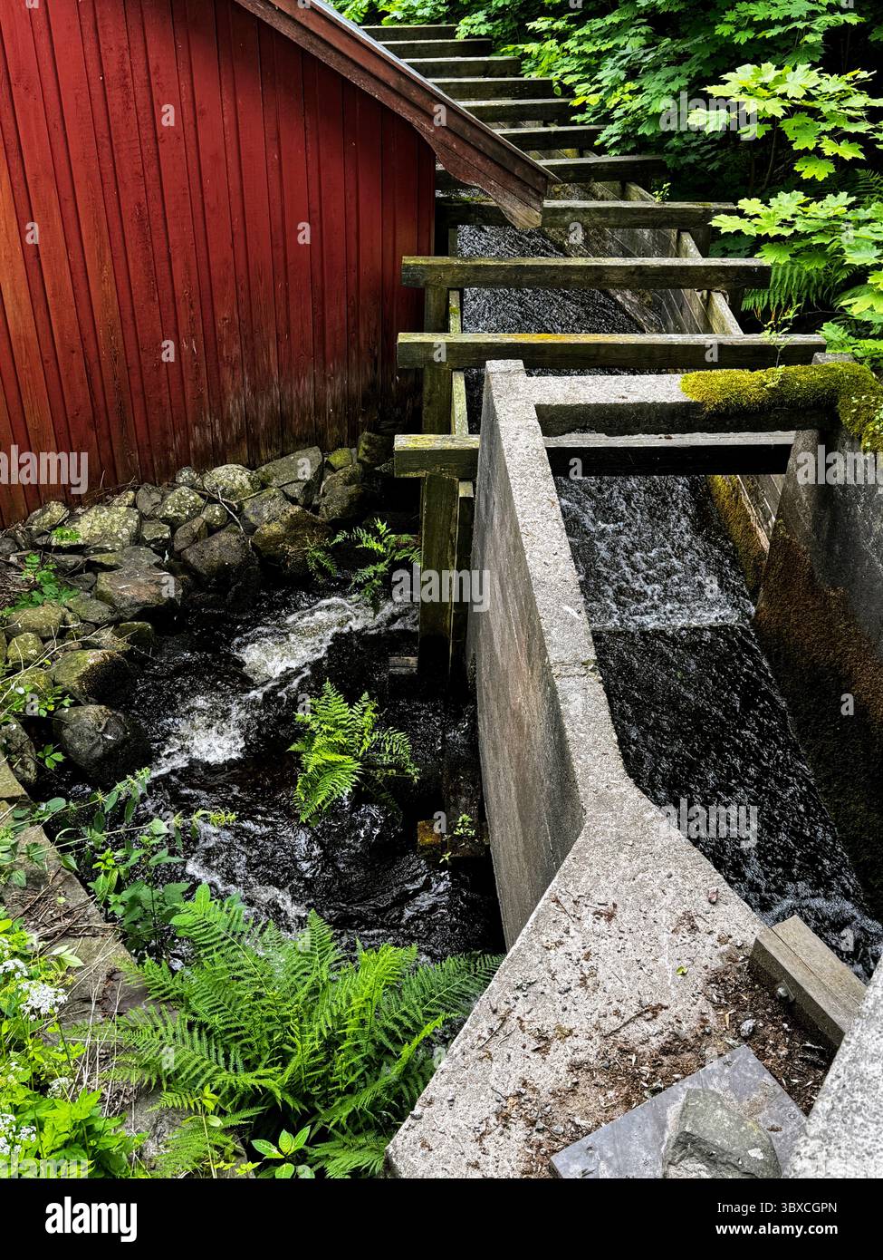 Historischer Damm und rote Scheune mit weichem Wasserfluss, Fagervik, finnische Natur und Industriegeschichte kombiniert. - Smartphone-aufgenommenes Stockfoto