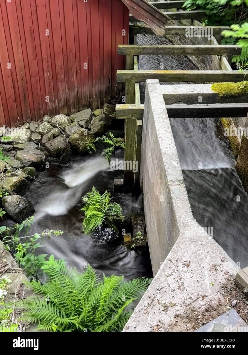 Historischer Damm und rote Scheune mit weichem Wasserfluss, Fagervik, finnische Natur und Industriegeschichte kombiniert. - Smartphone-aufgenommenes Stockfoto