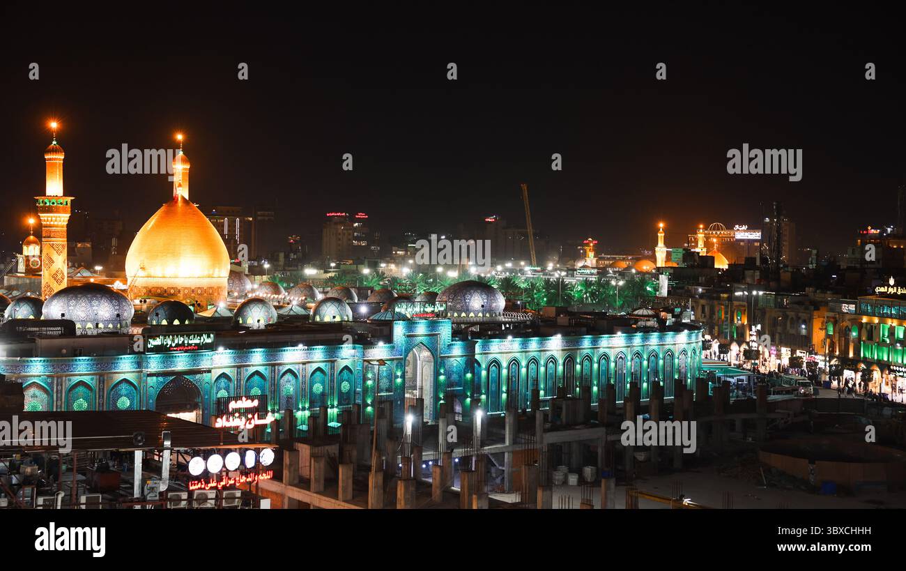 Karbala zeigt den beleuchteten heiligen Schrein bei Nacht, leuchtende grüne und goldene Lichter beleuchten die Gegend, umgeben von einer geschäftigen Stadt. Stockfoto