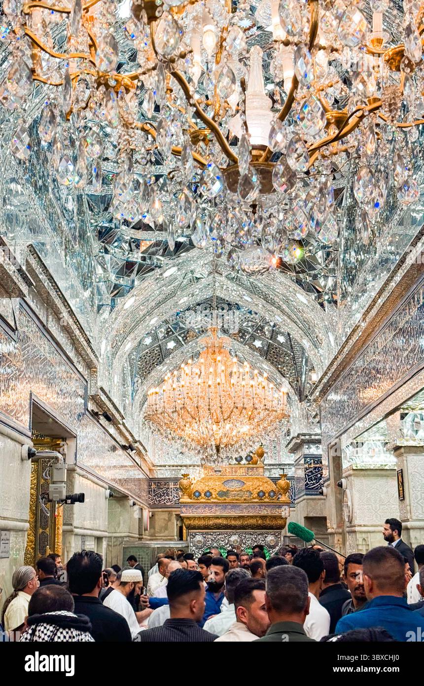 Die Menschen versammeln sich im kunstvollen Karbala-Schrein, gefüllt mit atemberaubenden Kronleuchtern und Dekorationen, für ein bedeutendes Ereignis. Stockfoto