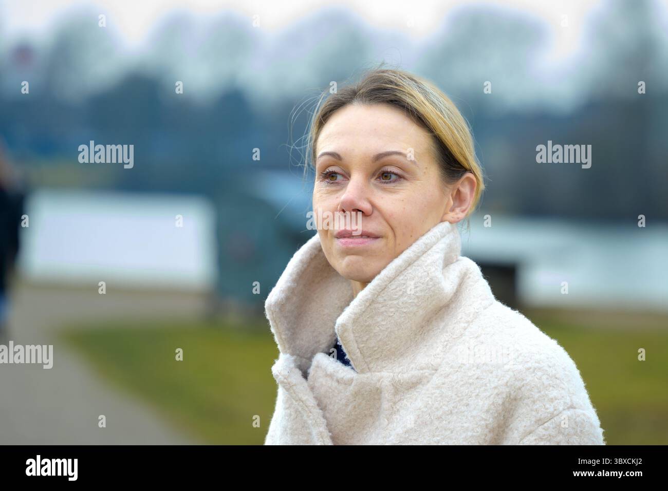 Eine Frau in einem cremefarbenen Mantel mit hohem Kragen steht draußen an einem kühlen Tag. Stockfoto