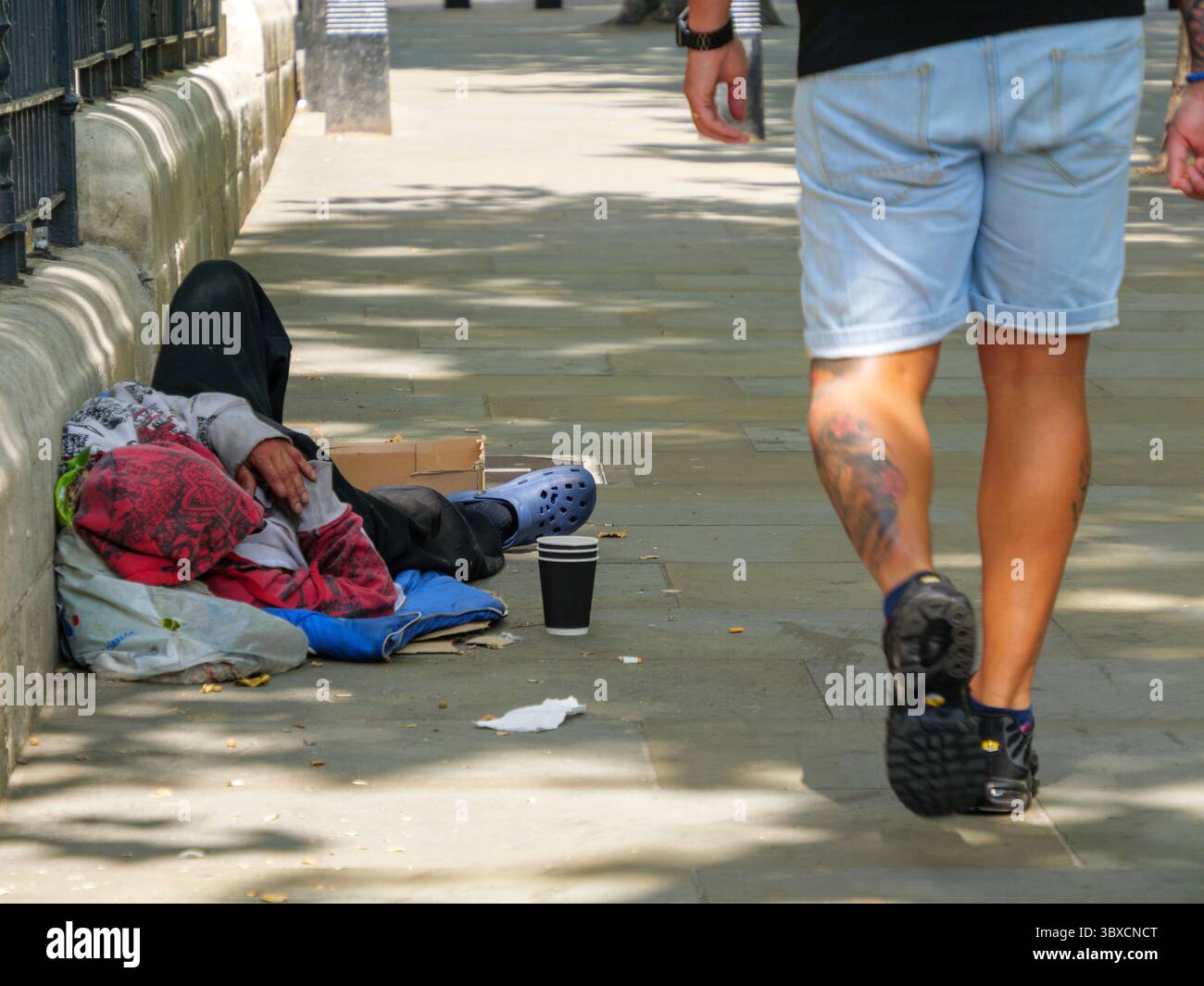 Fußgänger gehen an einem Obdachlosen vorbei, der auf einer belebten Londoner Straße neben einem Becher für Spenden liegt, was die zunehmende Sichtbarkeit von Obdachlosigkeit und wirtschaftlicher Not in der britischen Hauptstadt unterstreicht. Stockfoto Fußgänger gehen an einem Obdachlosen vorbei, der auf einer belebten Londoner Straße neben einem Becher für Spenden liegt, was die zunehmende Sichtbarkeit von Obdachlosigkeit und wirtschaftlicher Not in der britischen Hauptstadt unterstreicht. Stockfoto