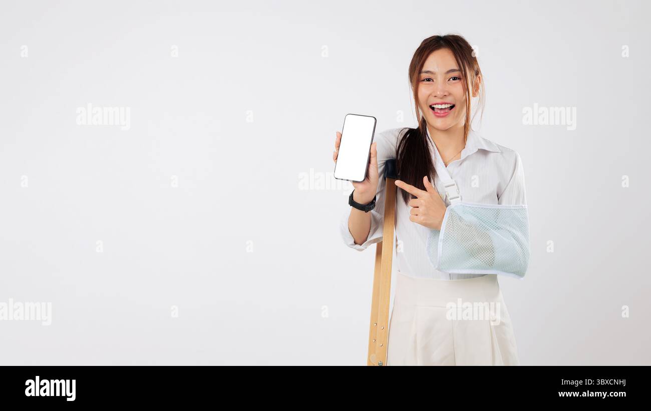 Verletzte asiatische Frau mit gebrochenem Arm, in einem Gips, das Telefon hält, benutzt mobile Unterstützung Stockfoto