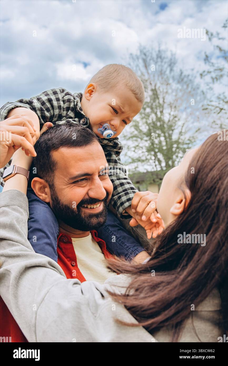 Nahaufnahme einer Familie, ein Kleinkind sitzt auf Papas Schultern, weint und geht zu Mom. Sie hält sanft seine Hände und versucht, ihn zu trösten. Ein berührendes Mo Stockfoto