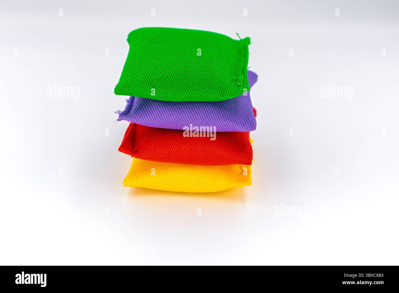 Vier bunte Sitzsäcke in Grün, Lila, Rot und Gelb sind ordentlich gestapelt und bereit für unterhaltsame und lehrreiche Aktivitäten. Stockfoto
