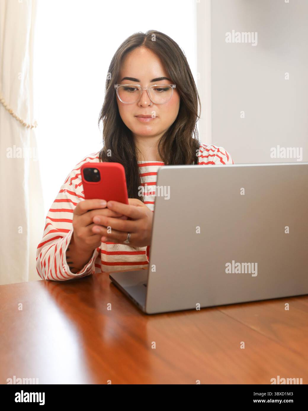 Junge Frau, die ihr Smartphone benutzt, während sie von zu Hause aus arbeitet Stockfoto