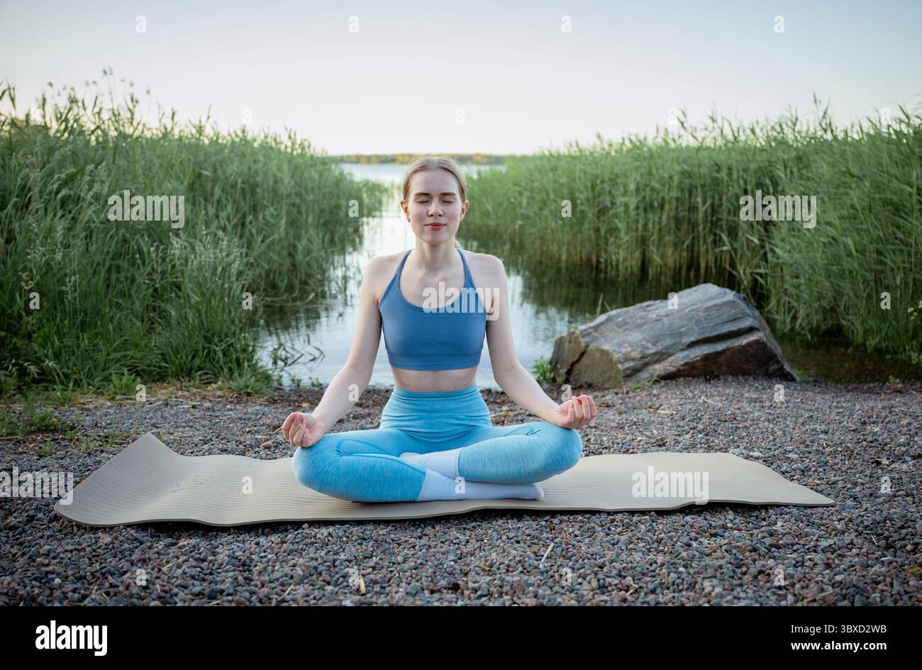 Junge Frau, die an einem Sommertag in der Nähe eines Sees Yoga-Übungen praktiziert Stockfoto