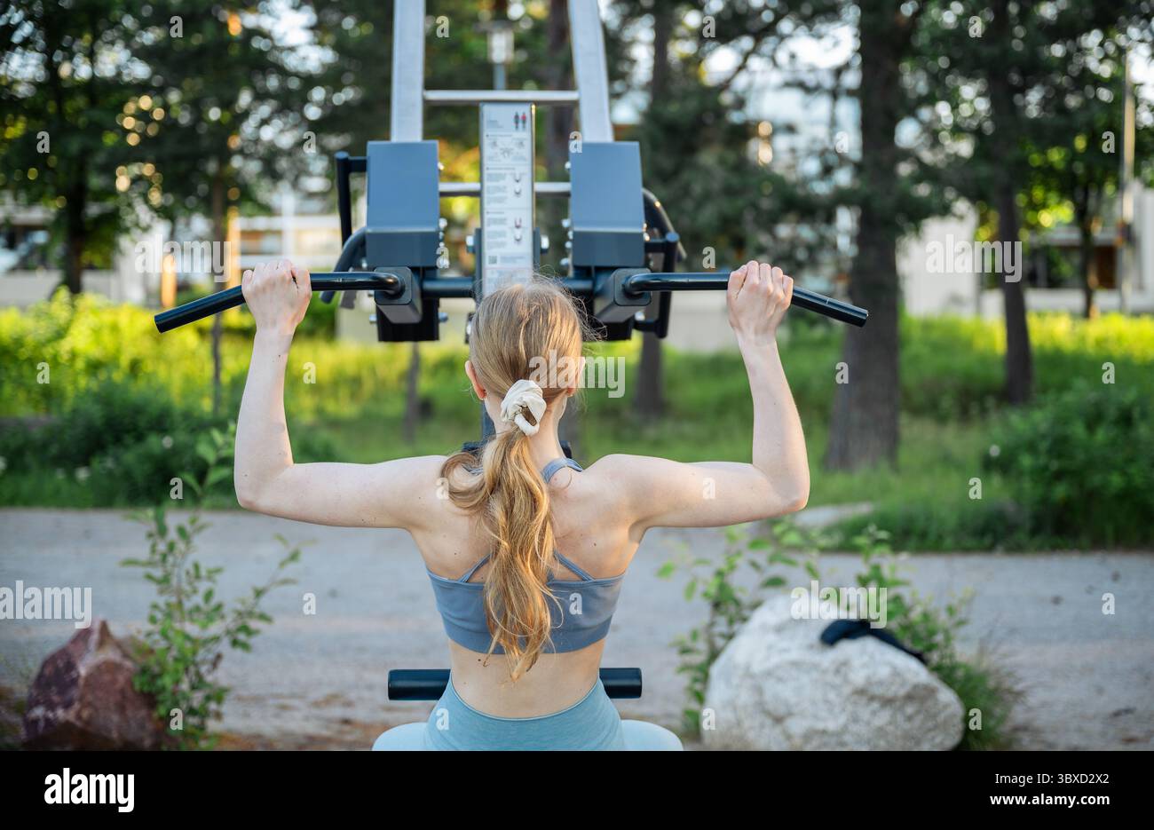 Frau, die im Sommerpark im Outdoor Gym ein Lat-Pull-Down-Gerät benutzt Stockfoto