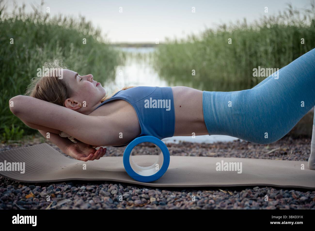 Frau, die auf Schaumstoffrolle für Rückenmassage beim Outdoor-Sommertraining liegt Stockfoto