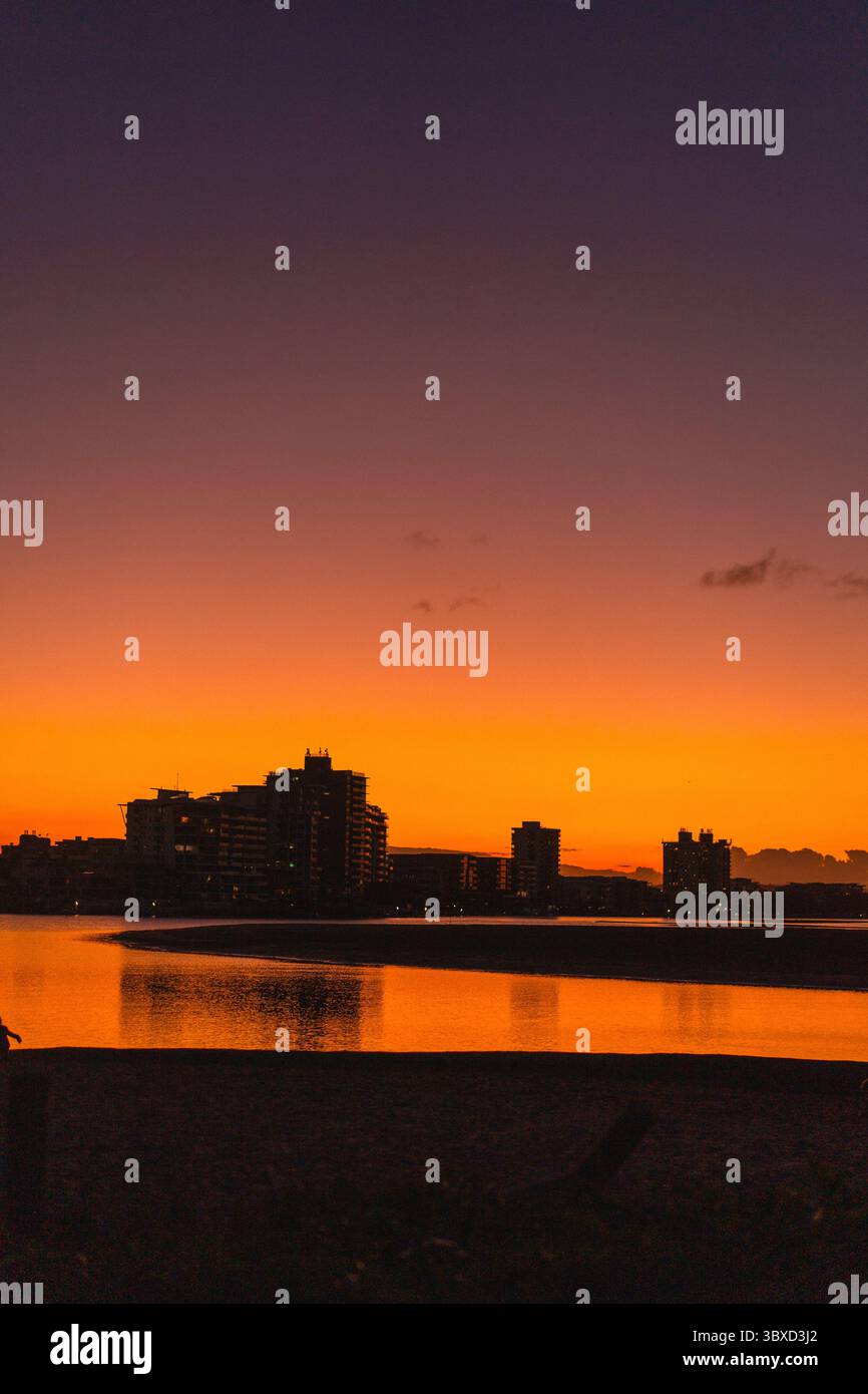 Skyline der Stadt bei Sonnenuntergang, Reflexionen, leuchtender orange und lila Himmel Stockfoto