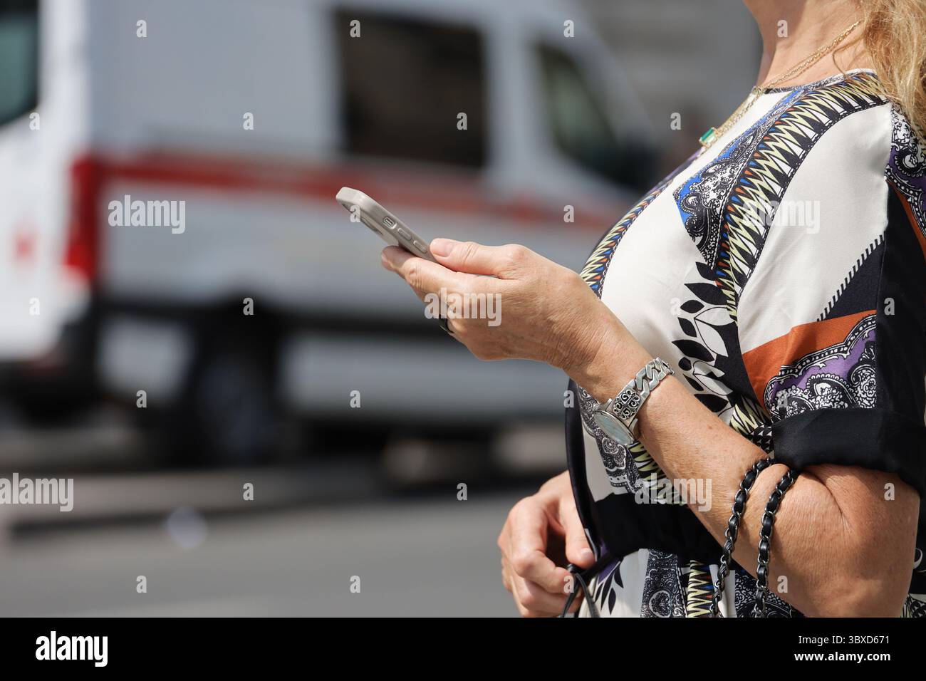 Smartphone in weiblichen Händen auf der Straße. Frau, die das Handy benutzt, steht auf dem Hintergrund eines Krankenwagens Stockfoto