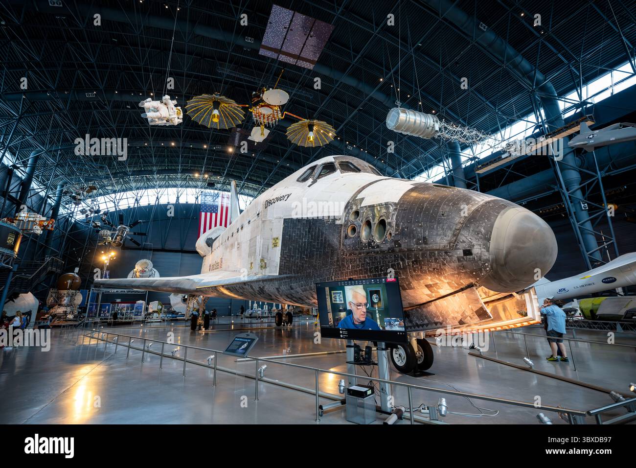 Space Shuttle Discovery-Ausstellung im Steven F. Udvar-Hazy-Zentrum in Chantilly, Virginia | CHANTILLY, Va. — Besucher versammeln sich unter der Nase und dem offenen Laderaum des Space Shuttle Discovery im Steven F. Udvar-Hazy-Zentrum in Chantilly, Virginia, wo Satellitenmodelle und eine Astronautenpuppe für einen Weltraumspaziergang über ihnen hängen. Discovery flog 39 Missionen zwischen 1984 und 2011, mehr als jeder andere Orbiter, einschließlich des ersten Shuttle-Dockens mit der Internationalen Raumstation im Jahr 1999. Die NASA bewahrte es in seinem geflogenen Zustand als ihr designiertes „Fahrzeug der Aufzeichnung“ auf. Stockfoto