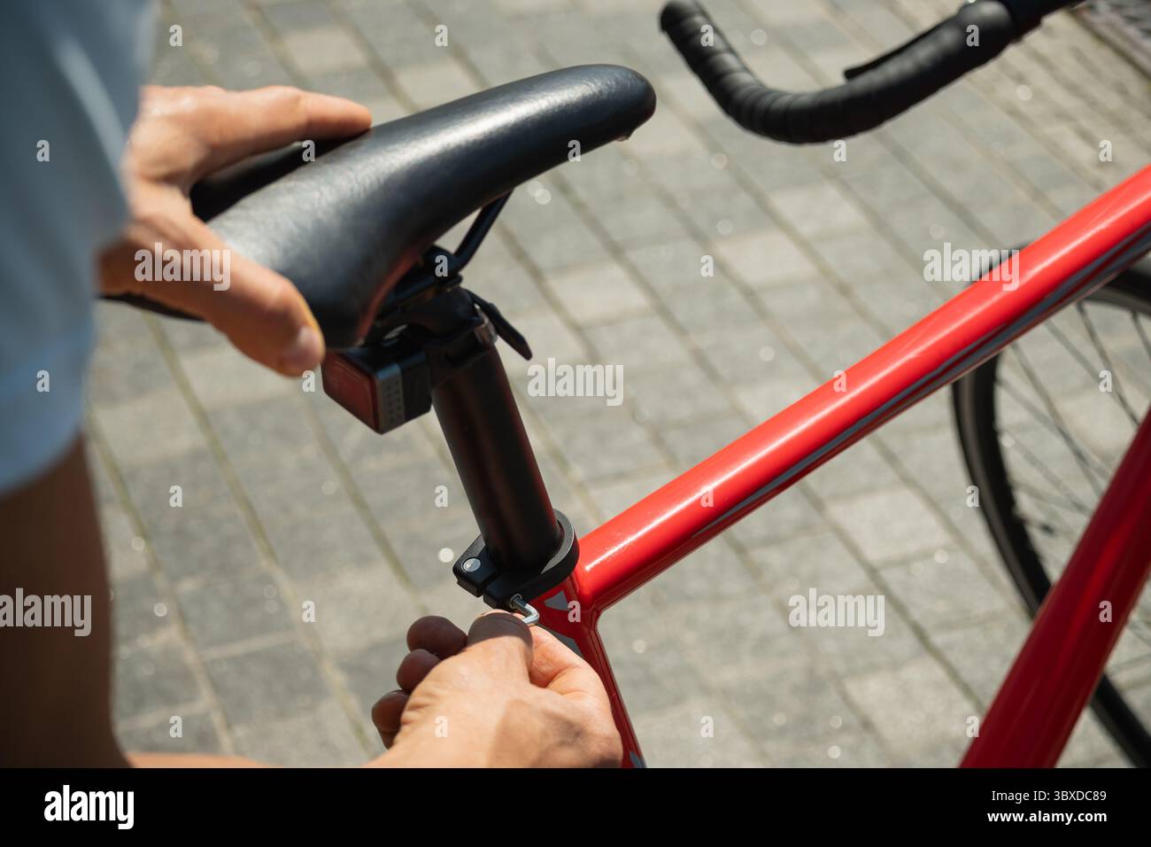 Bei Nahaufnahme der Hände wird der rote Fahrradsitz mit dem Sechskantschlüssel verstellt, um eine komfortable Fahrt zu gewährleisten. Fahrradmechaniker, der das Brems- und Schaltsystem von Fahrrad A zusammenbaut Stockfoto