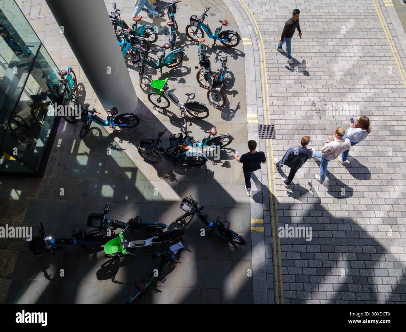Fußgänger bewegen sich in der City of London, Großbritannien, um zahlreiche Mietfahrräder herum, die auf dem Bürgersteig herumlaufen, was die wachsende Besorgnis über die Behinderung des öffentlichen Raums durch Fahrräder ohne Dock hervorhebt. Stockfoto