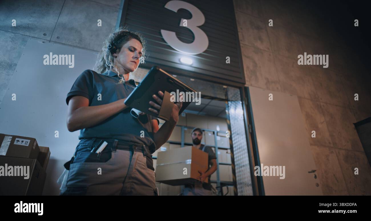 Weibliche Manager scannt Pakete mit Barcode-Scanner mit Digital Tablet. Verschiedene Mitarbeiter, die nachts Kartons aus dem Logistics Distribution Warehouse transportieren. Online-Bestellungen, Waren, Lieferung. Stockfoto