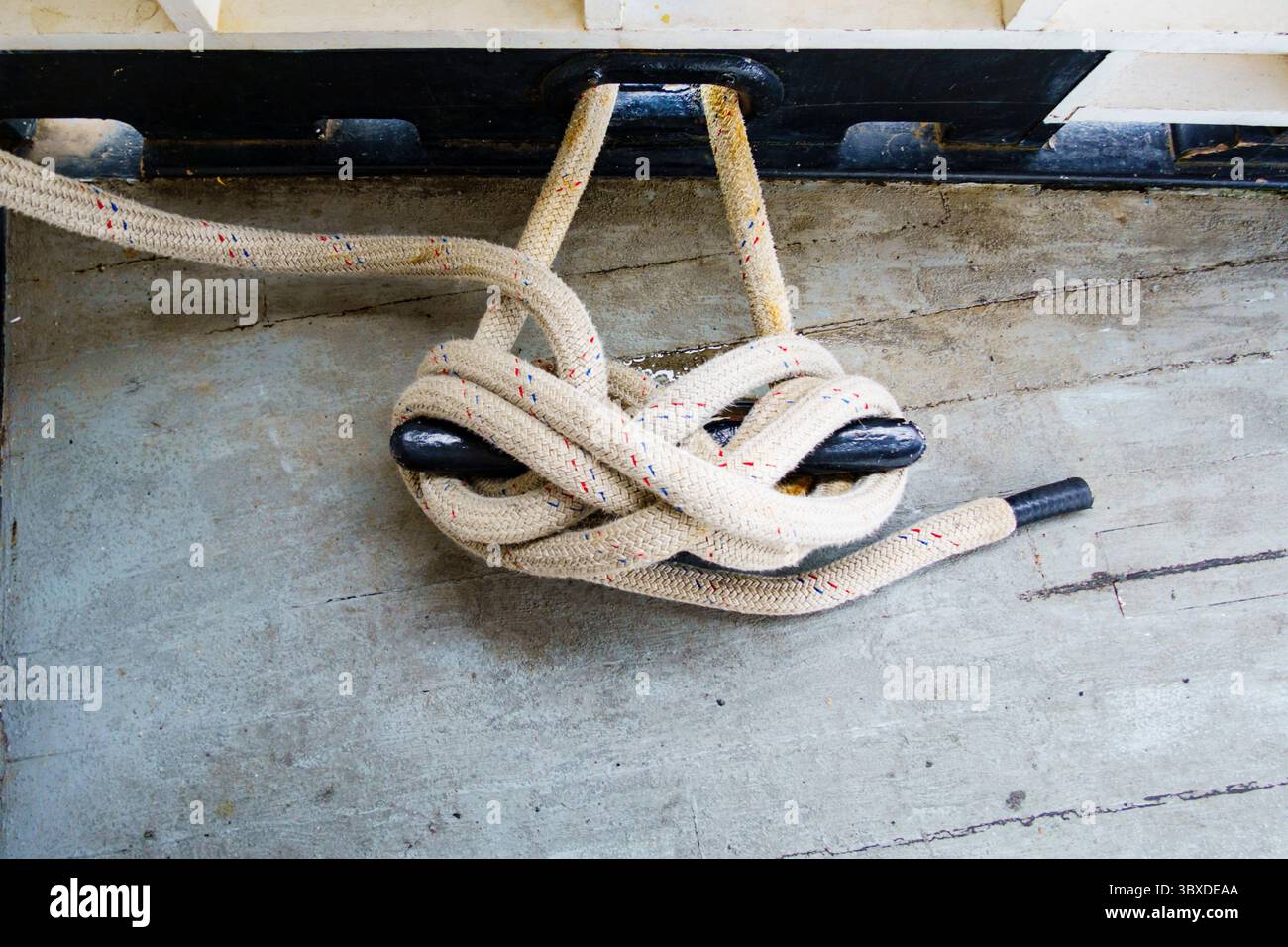 Ein Seil, das um eine Metallklammer auf dem Schreibtisch eines Schiffes befestigt ist, sicheres Anlegeseil, Nahaufnahme. Stockfoto