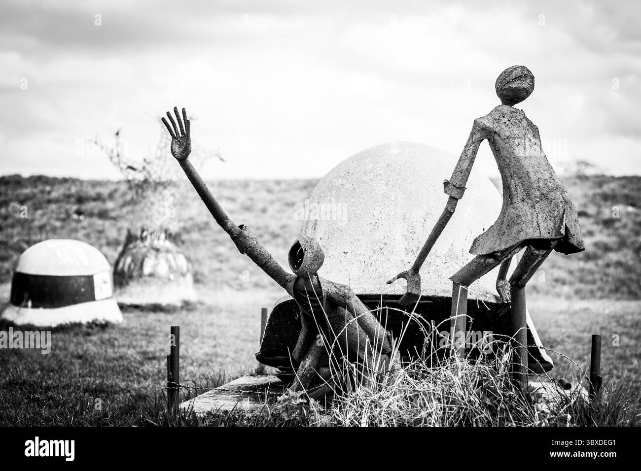 Auffälliges Schwarzweiß-Bild mit zwei verwitterten, abstrakten Metallskulpturen vor einem riesigen, einsamen Grasfeld unter einem dramatischen Himmel. Stockfoto