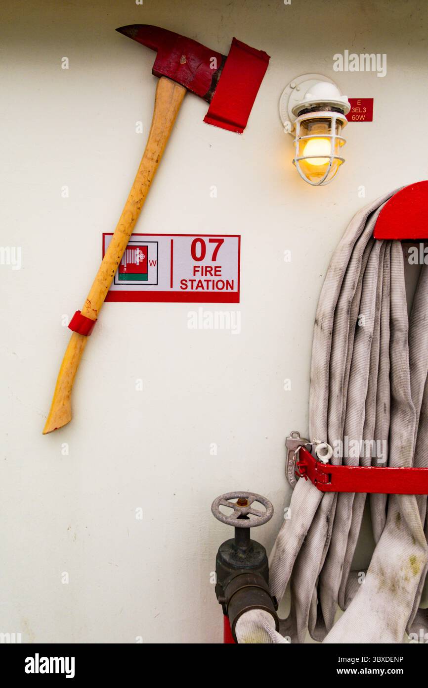 Feuerwehrausrüstung, rote Axt und Wasserschlauch an der Wand und eine Alarmtafel. Stockfoto