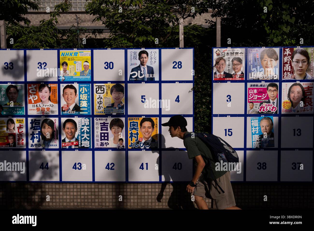 A pedestrian passes an election board displaying posters of candidates for the upcoming July 20 upper house election in Tokyo, Friday, July 18, 2025. (AP Photo/Louise Delmotte) Stockfoto
